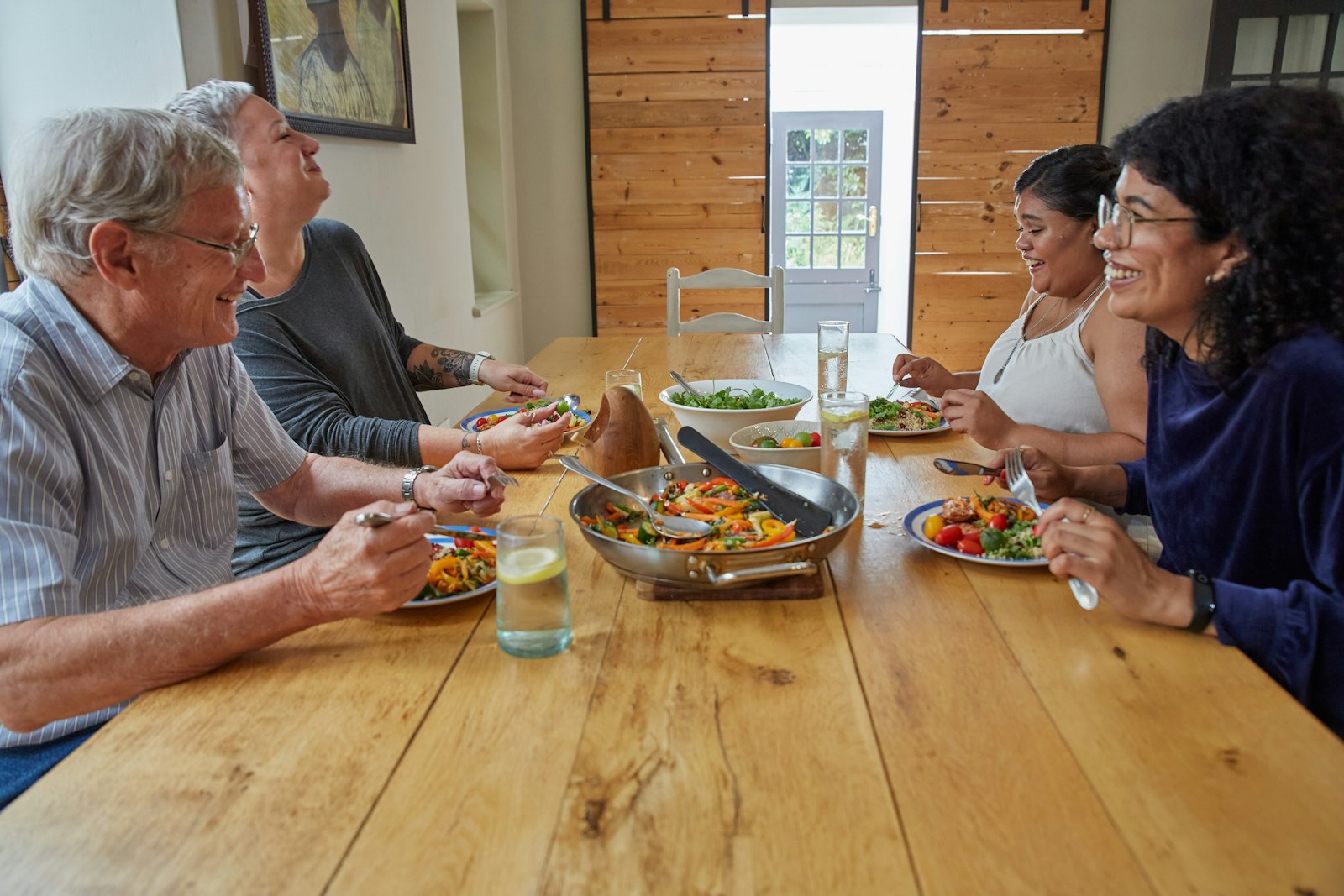 An older couple at a family dinner table, laughing with their adult children